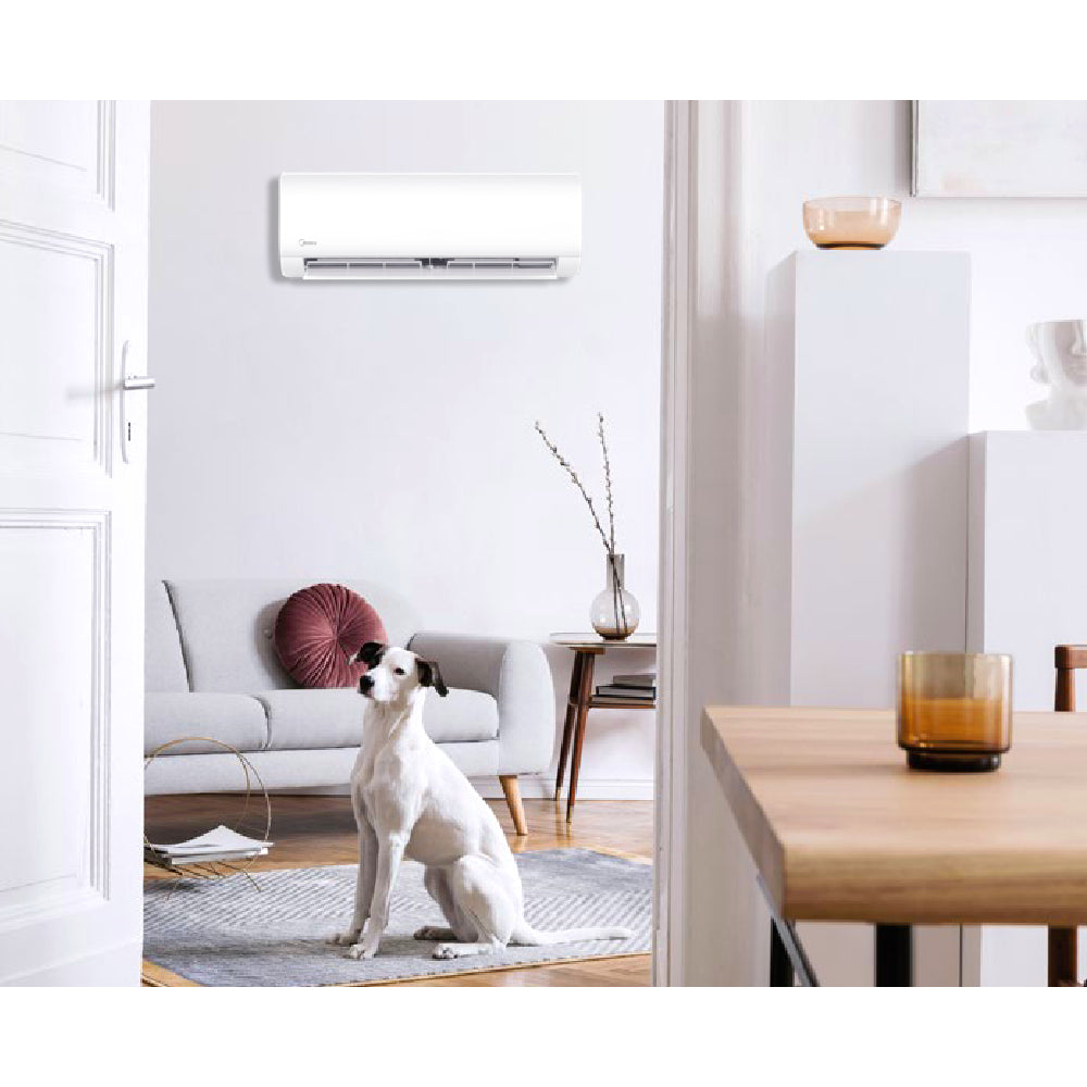 MIDEA XTREME SAVE BLUE | Innengerät im modernen Wohnzimmerambiente, ein Hund sitzt im Raum auf einem Teppich. Foto von einem Nebenraum durch die geöffnete Tür fotografiert.